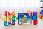 TileTek magnetic square tiles shown with a colorful assembled structure on the left, the product box in the center, and stacked translucent tiles on the right, photographed in a bright indoor room.